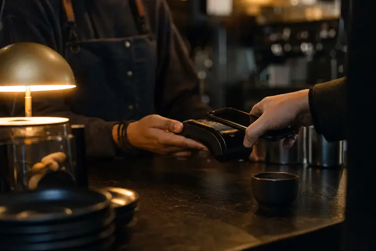 A customer tapping a card on a terminal at a cafe counter